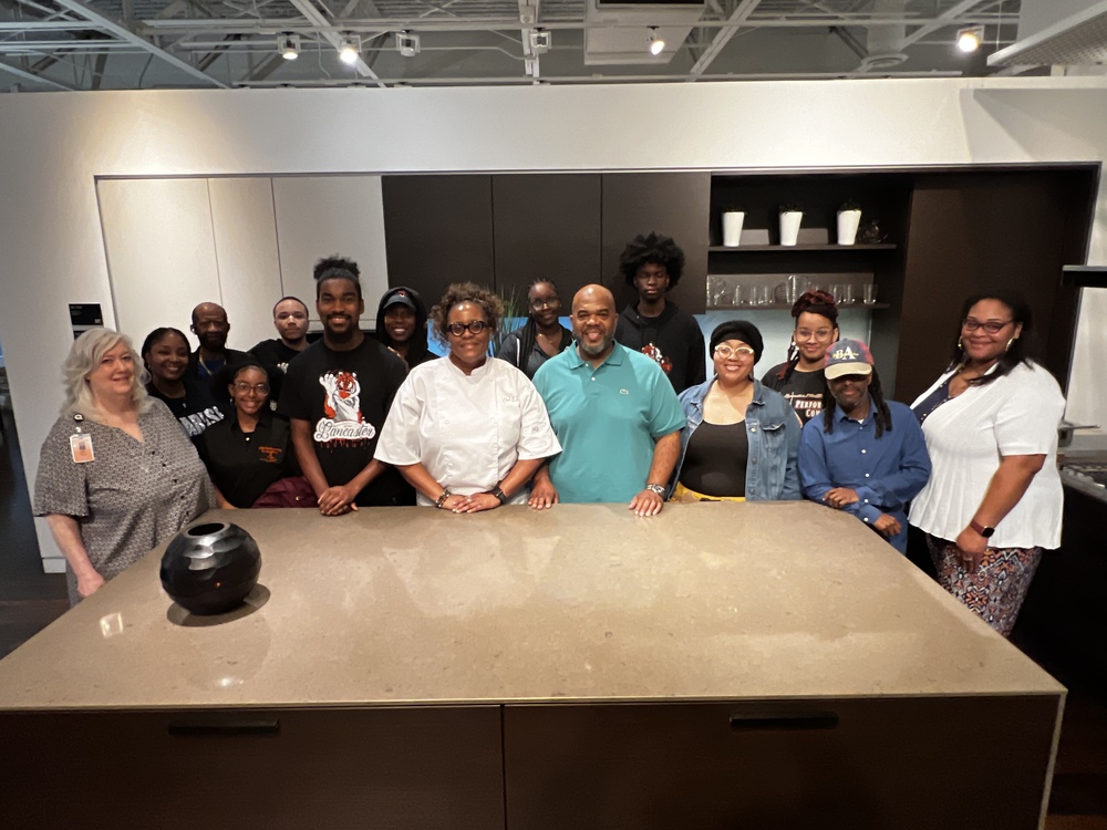 Students and teachers stand smiling in a studio kitchen